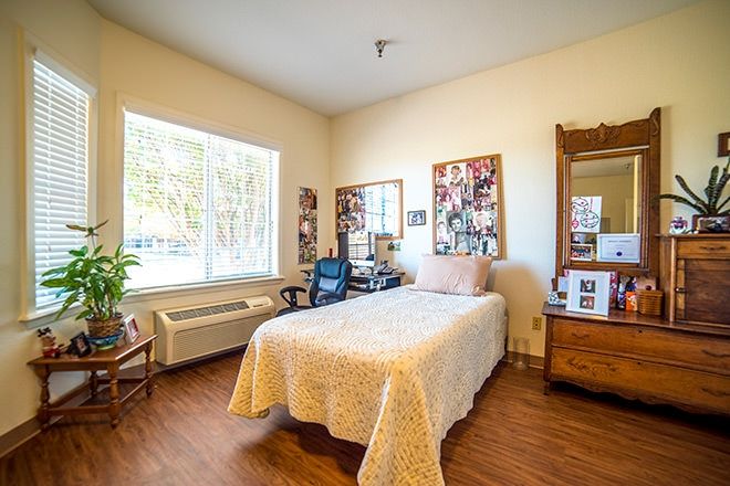 A cozy bedroom with a single bed, decorated with photographs and featuring a desk chair by the window.