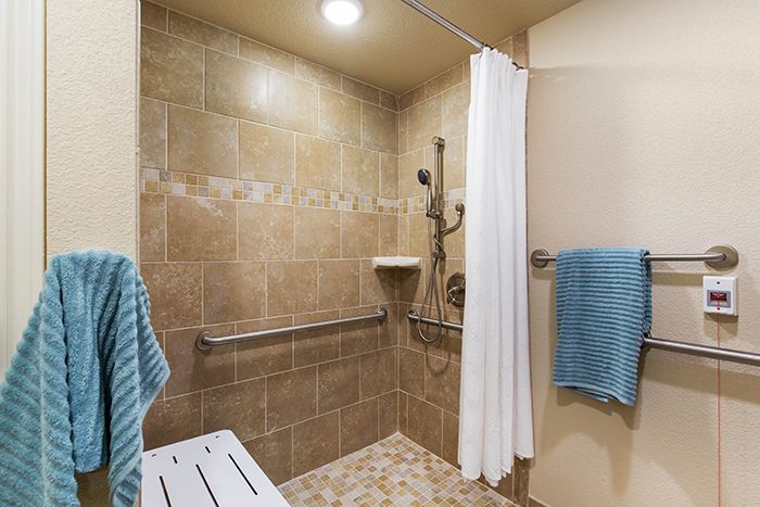 A modern walk-in shower with tiled walls, equipped with grab bars and a bench seat for accessibility.