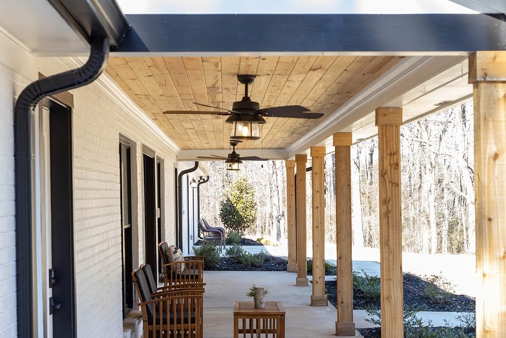 A cozy covered porch with wooden furniture and ceiling fans.