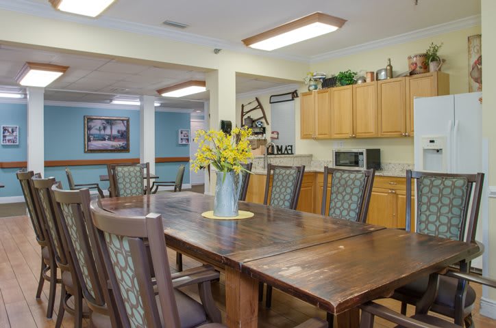 A cozy dining area with a large wooden table and chairs, adorned with a vase of yellow flowers.