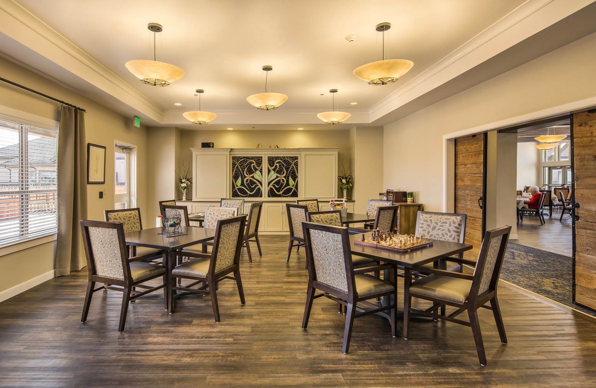 A well-lit dining room with multiple tables and chairs, featuring elegant lighting fixtures and a wooden floor.