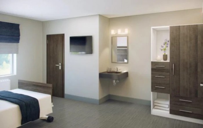 A modern hospital room with a bed, wall-mounted television, sink, and cabinetry.