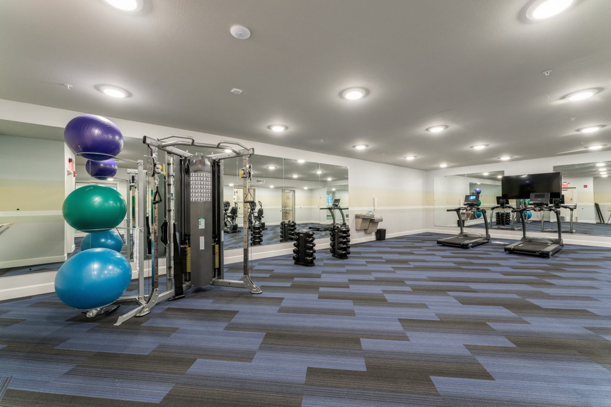 A spacious gym with various exercise equipment, including treadmills and weights, surrounded by large mirrors.