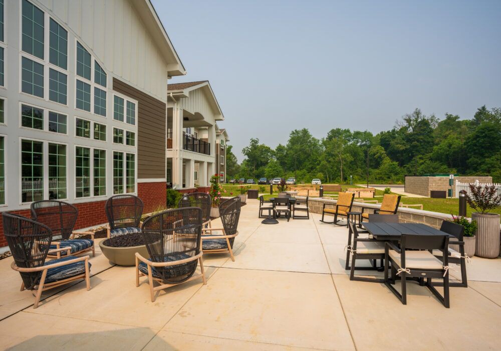 An outdoor patio area with seating arrangements near a building, surrounded by greenery.