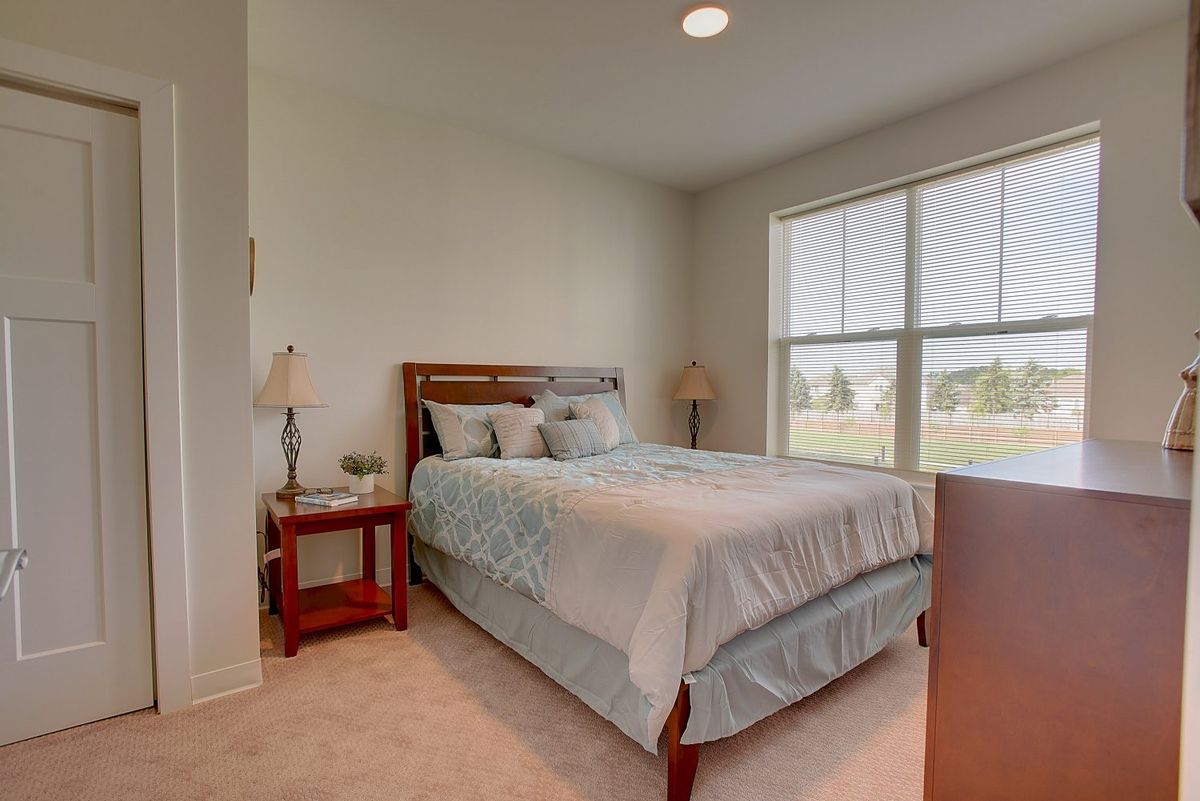 A cozy bedroom with a neatly made bed, bedside tables, and large windows allowing natural light in.