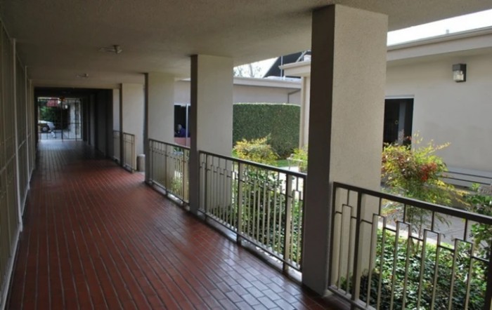 A covered outdoor corridor with railings overlooking a garden area.