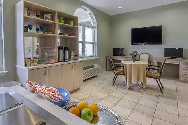A cozy kitchen and dining area with a TV, table and chairs, and a display of fruit.