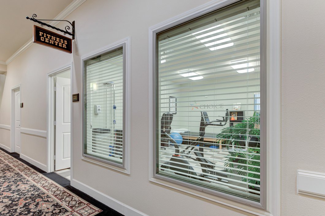 A view of an office interior with large windows and blinds, showcasing desks and chairs inside.