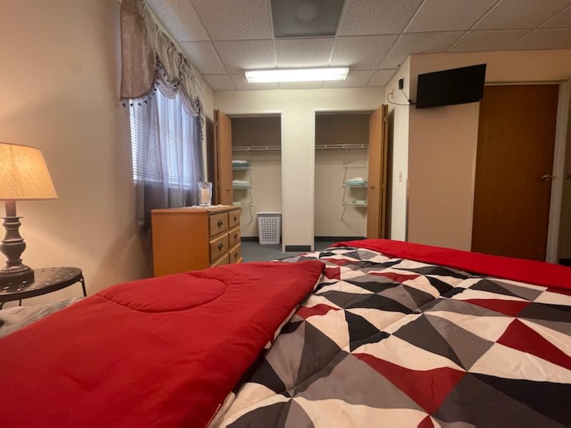 A view of a cozy bedroom with a neatly made bed, dual closets, and a dresser.