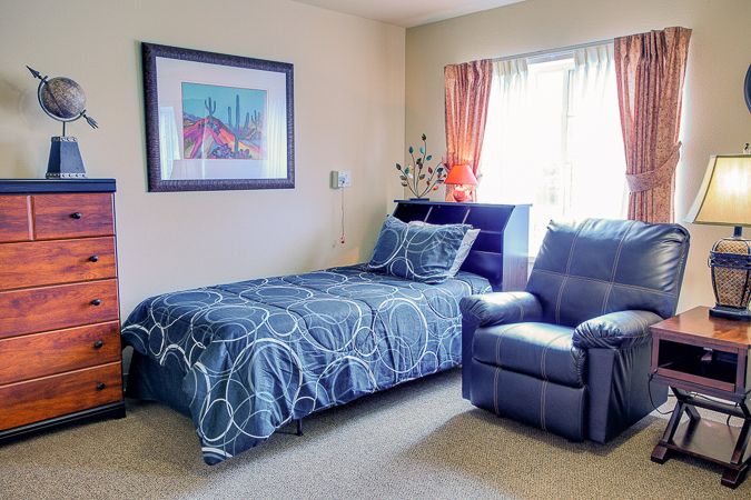 A cozy bedroom with a single bed, an armchair, and a decorative artwork on the wall.