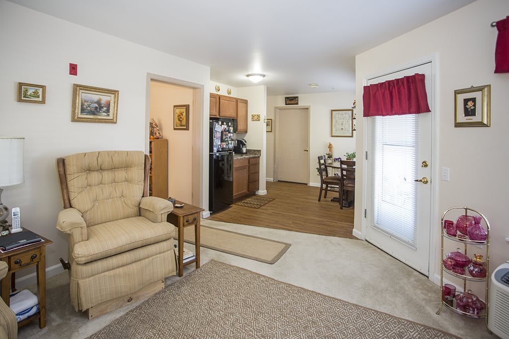 A cozy apartment interior featuring a living room with an armchair, connected to a small kitchen and dining area.
