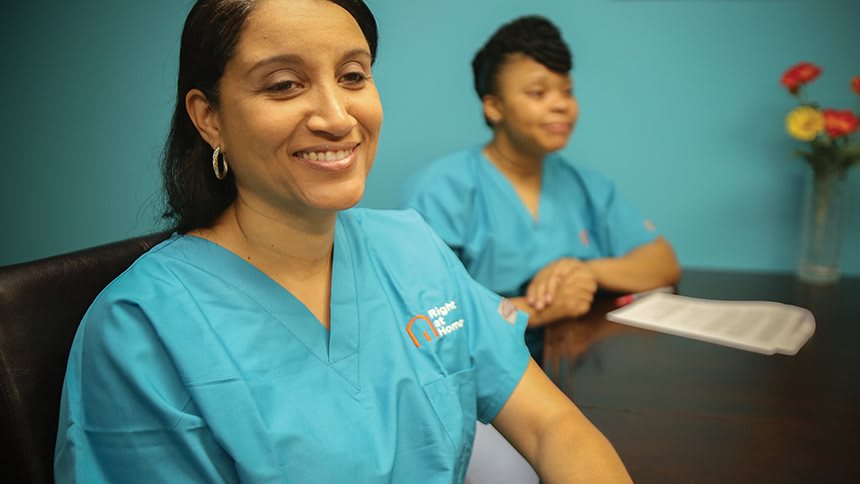 Two healthcare professionals in scrubs sit at a table, engaged in conversation.