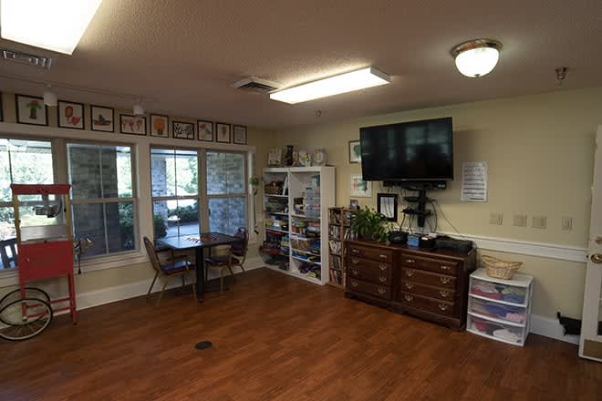 A cozy living room featuring a television, wooden flooring, and ample natural light.