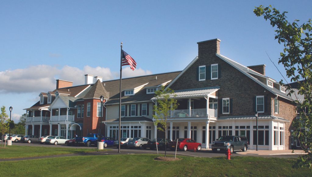 A large building with an American flag in front, surrounded by green grass and a clear sky.