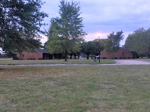 A serene view of a building surrounded by trees and open grass, under a cloudy sky.