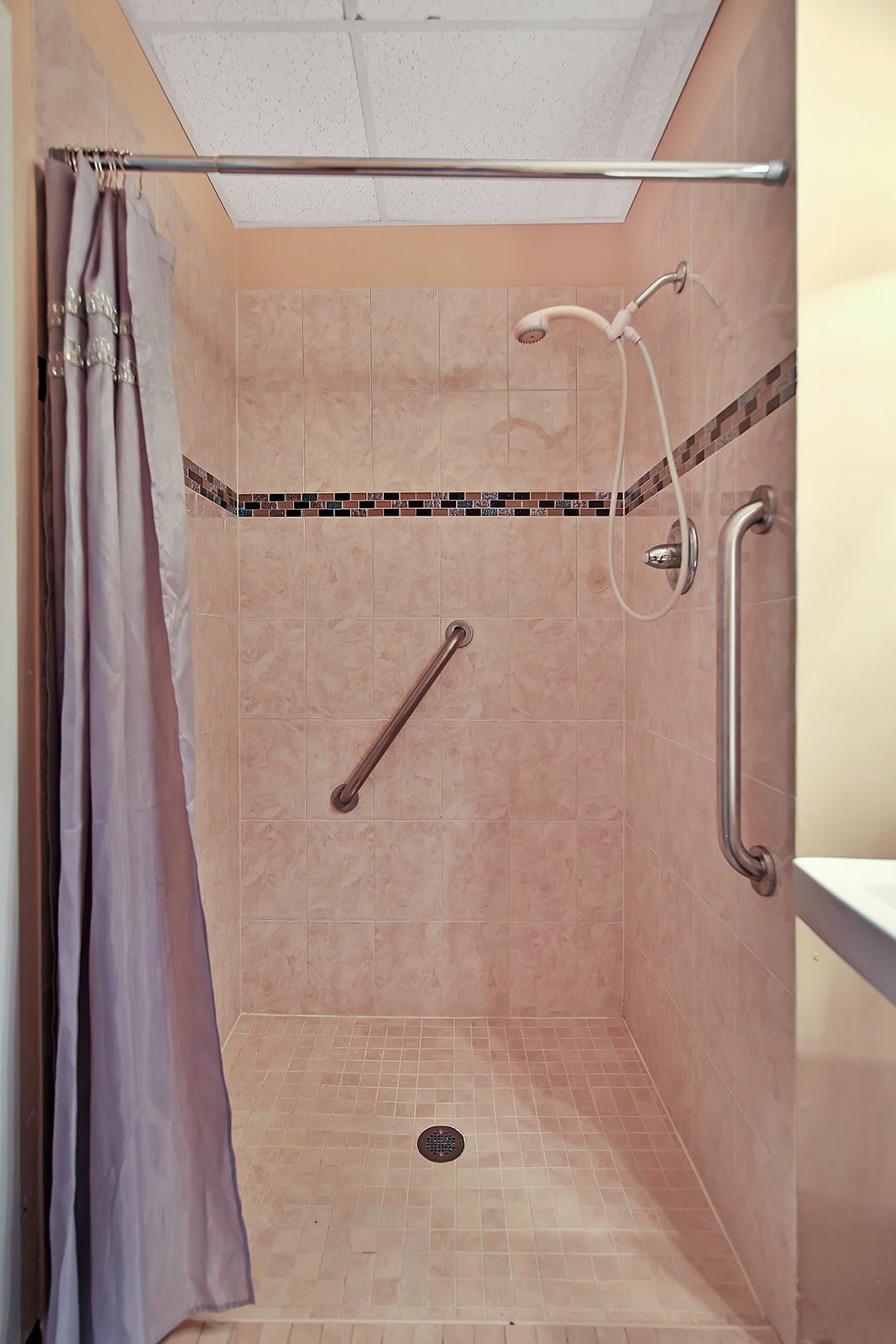 A tiled shower with grab bars and a curtain for safety and privacy.