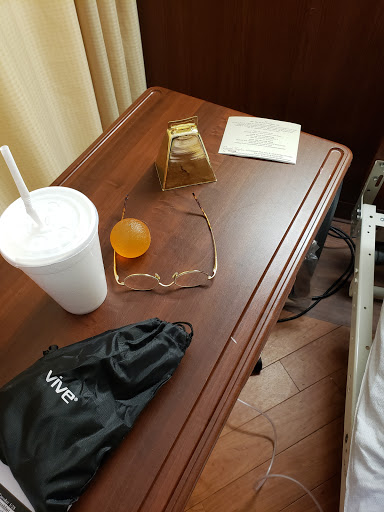 A bedside table with a drink, glasses, an orange ball, a note, and some miscellaneous items.