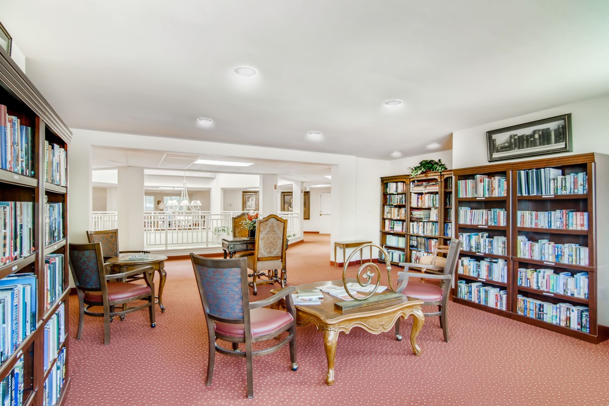 A cozy library space with bookshelves, tables, and chairs for reading.