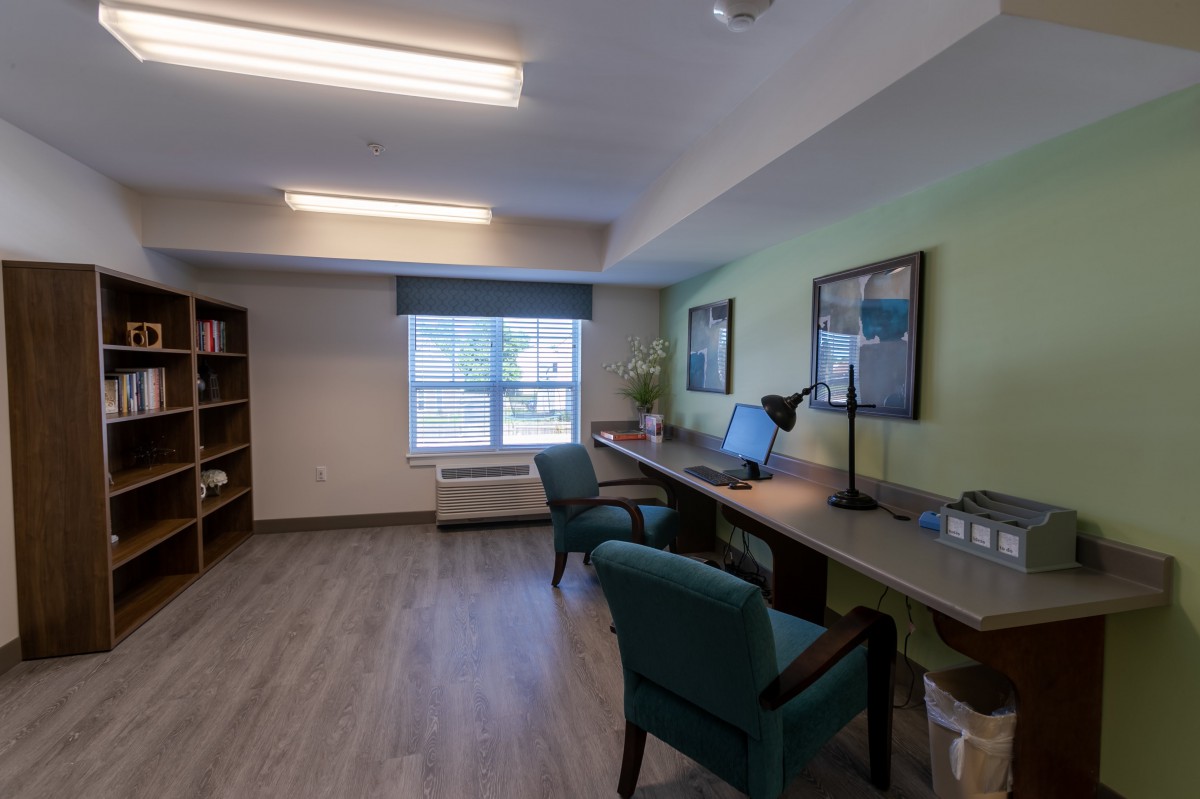 A tidy office space with a desk, chairs, computer, and bookshelf near a window.