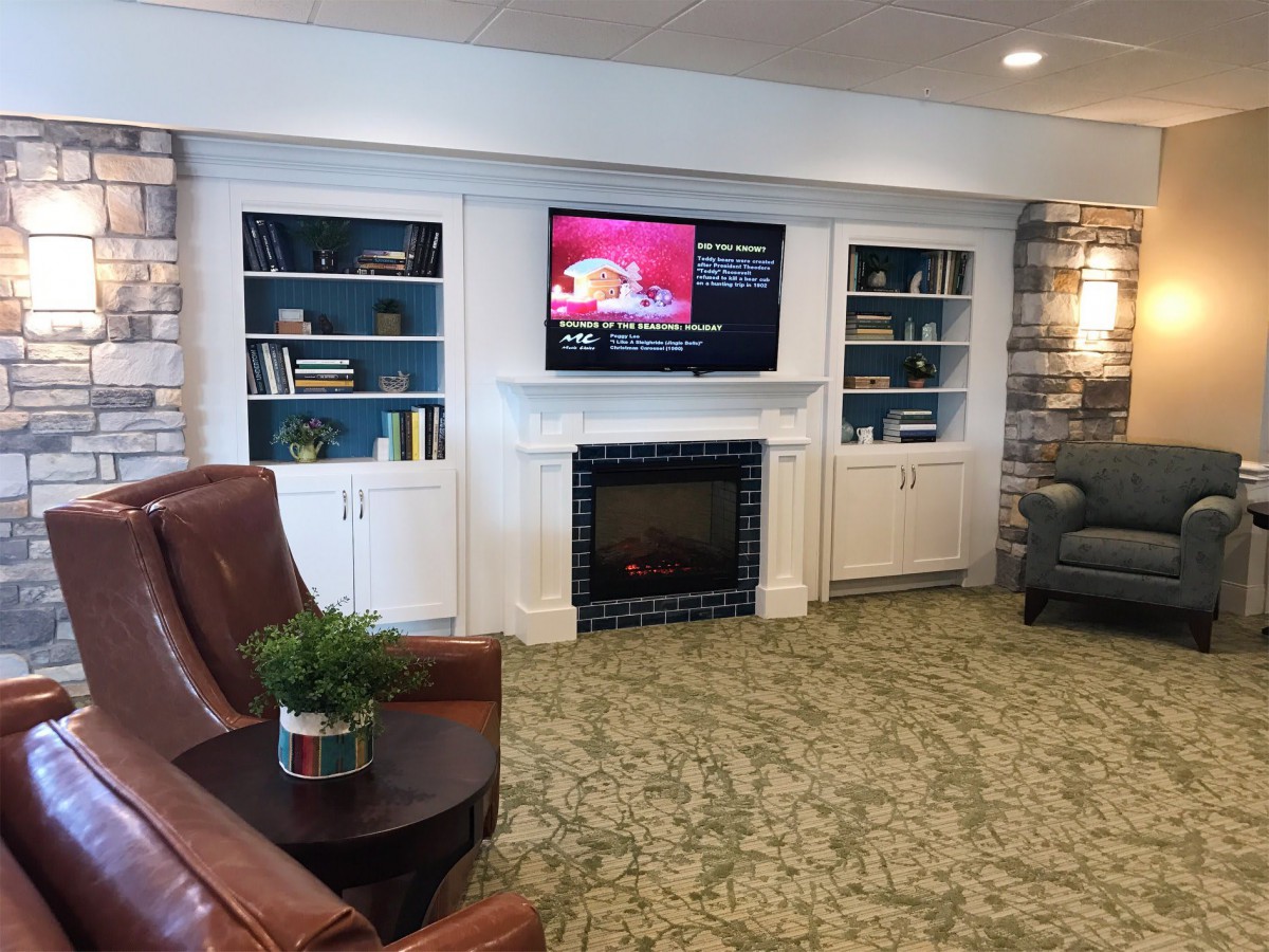 A cozy living room setting featuring a fireplace, built-in shelves with books, a flat-screen TV, and comfortable seating.