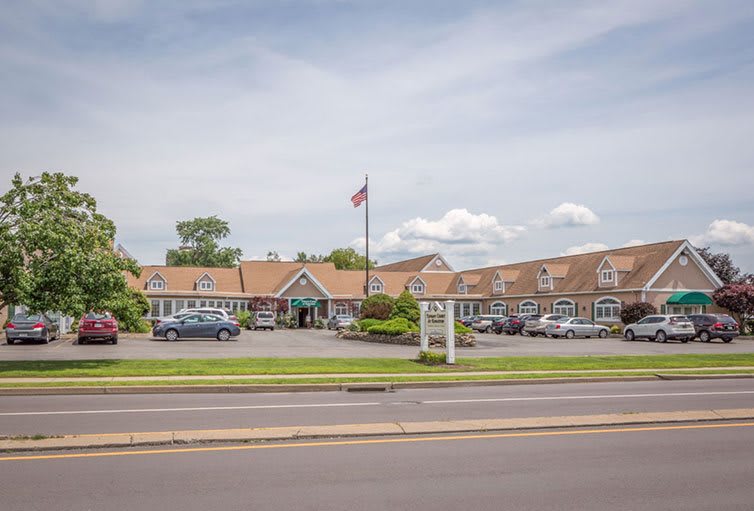 A roadside hotel with a parking area, flagpole, and clear sky.