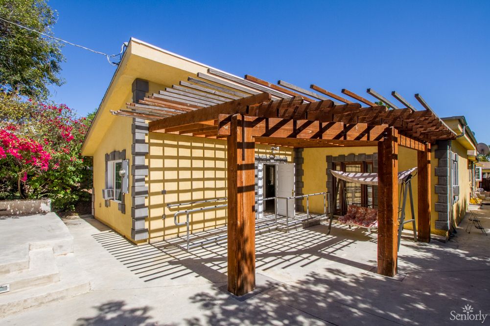 A yellow house with a wooden pergola on the patio.