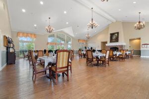 An elegant dining room with multiple tables and upholstered chairs, featuring chandeliers and a hardwood floor.
