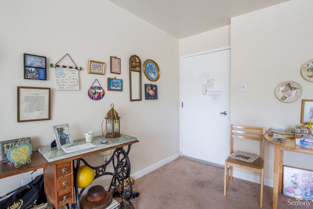 A cozy room with vintage decor, featuring a desk, wall art, and a chair near the door.