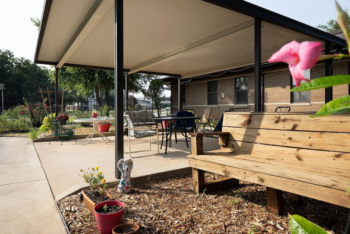 A cozy patio with a wooden bench and potted plants under a covered area.
