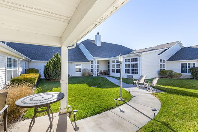 A serene outdoor patio and backyard area of a house with neatly maintained grass and seating.