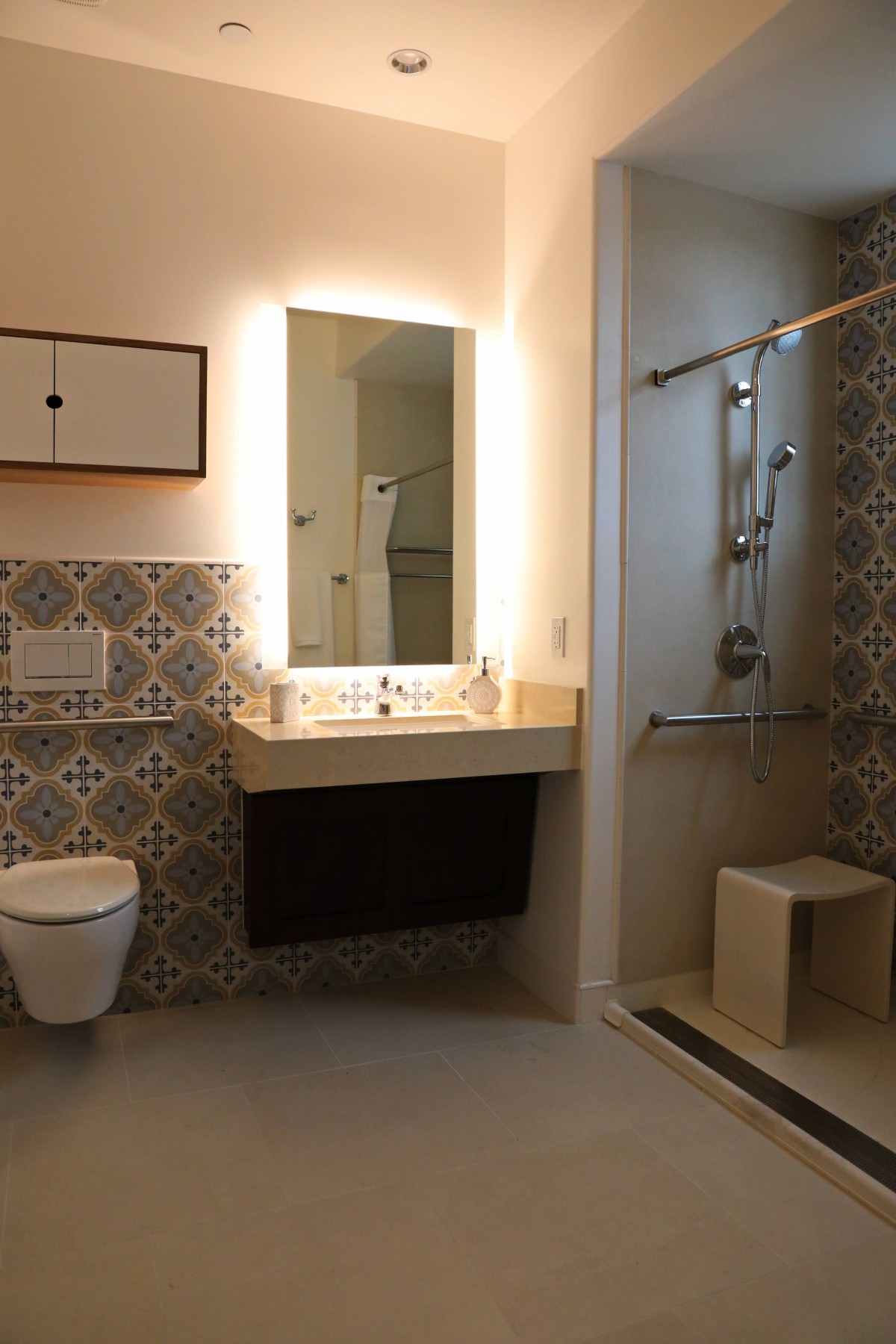 A modern bathroom with patterned tiles, featuring a sink, a large mirror, a toilet, and a walk-in shower.