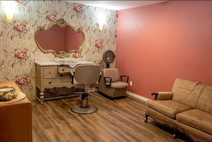 A vintage-themed salon with floral wallpaper, a large mirror, and retro furniture.