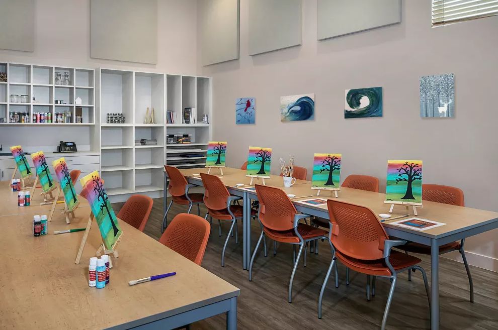 A classroom set up for an art class, featuring tables with art supplies and paintings on the wall.