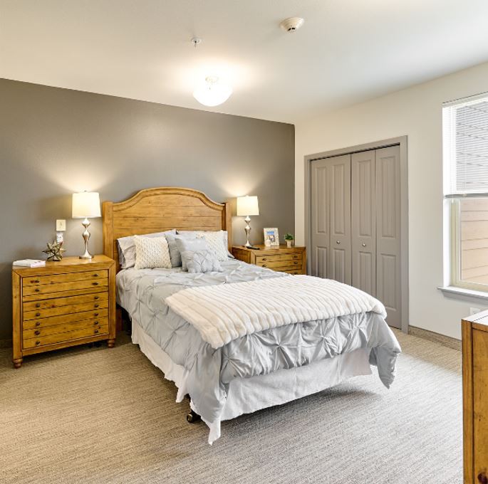 A cozy bedroom with a wooden bed frame and matching nightstands, featuring soft lighting and neutral decor.