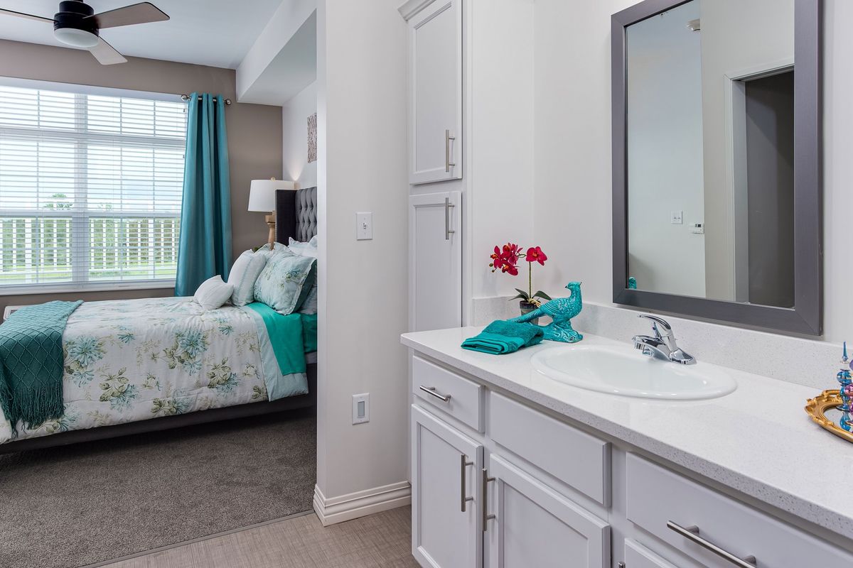 A modern bedroom and bathroom area featuring a sink with a mirror and floral decorations.