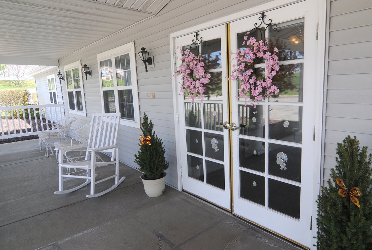 A charming porch with white rocking chairs, decorative wreaths on the doors, and potted plants.