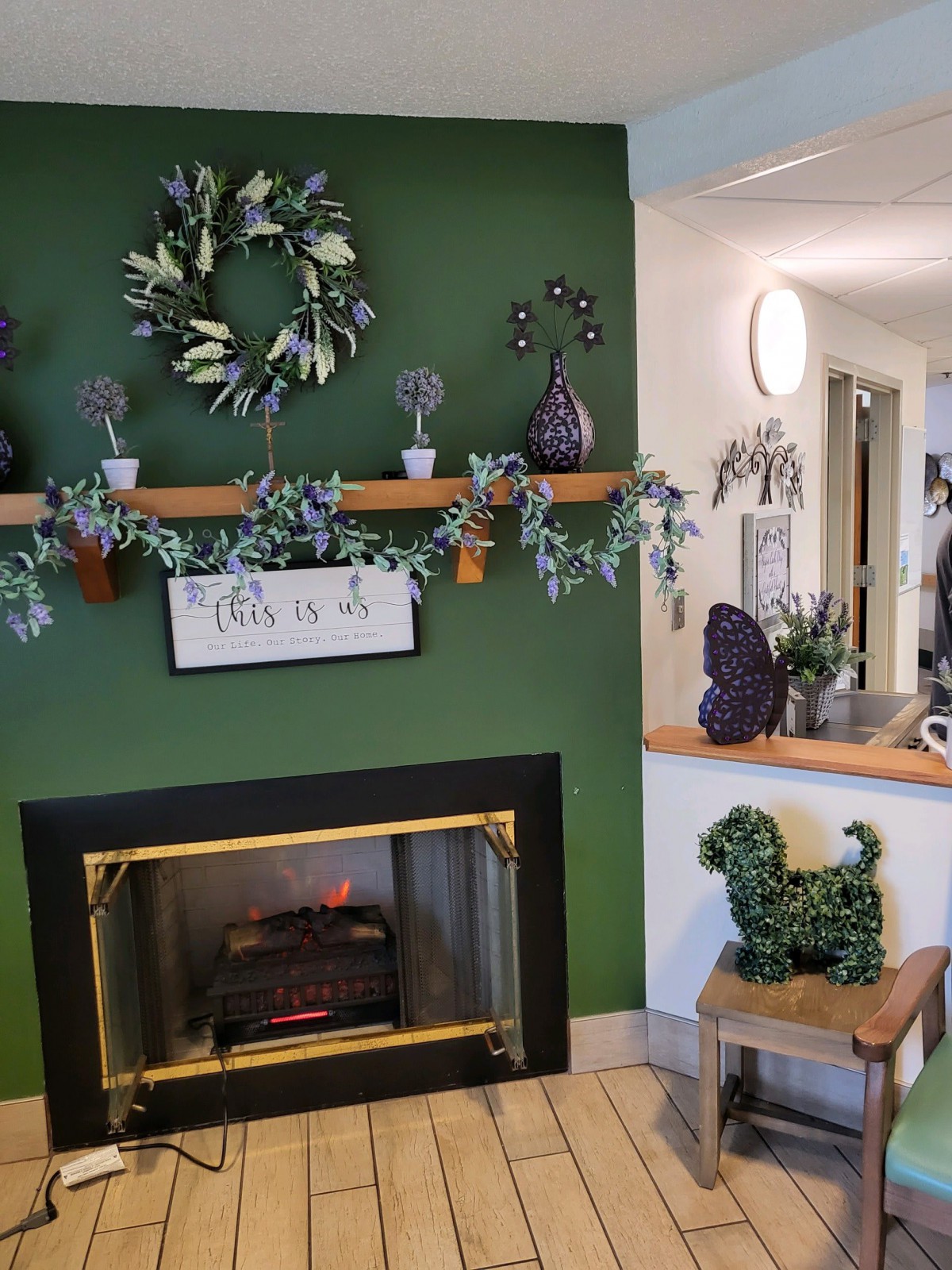 A cozy living room with a green accent wall featuring a decorated fireplace and mantel with wreaths and plants.
