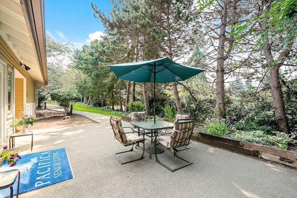 A tranquil patio area with a table and chairs under an umbrella, surrounded by lush greenery.