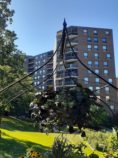 A unique sculpture hangs in a sunny park, overlooking an apartment building.
