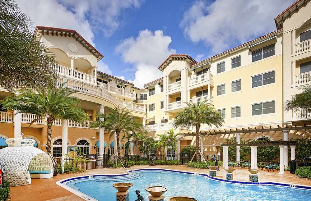 A tropical resort featuring a pool surrounded by palm trees and elegant architecture.