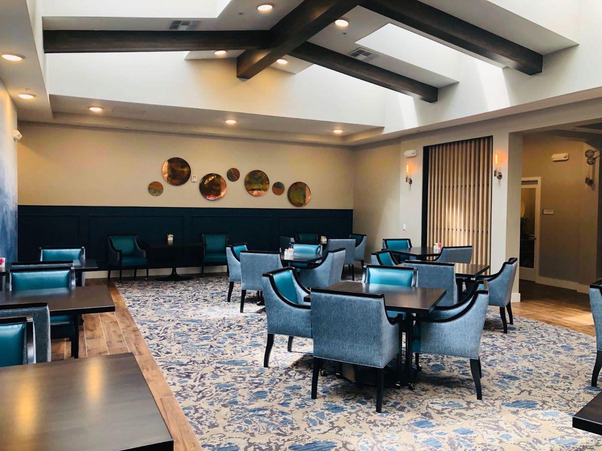 A modern dining area with blue chairs and a patterned carpet, featuring stylish decor and natural lighting.