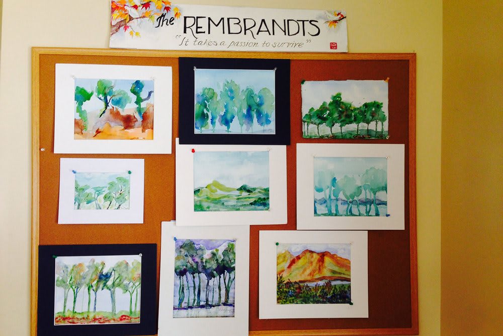 A collection of watercolor landscape paintings displayed on a bulletin board.