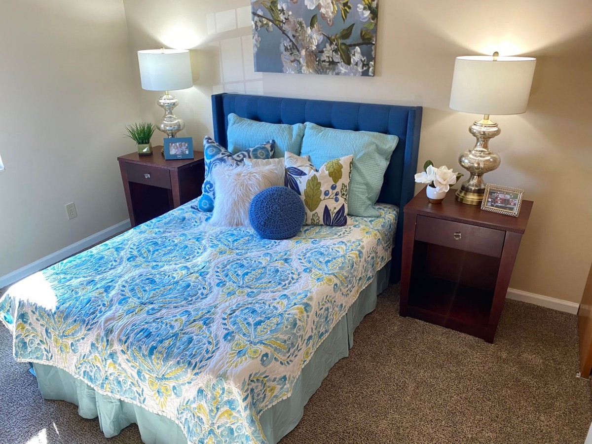 A cozy bedroom featuring a neatly made bed with colorful bedding and decorative pillows, flanked by two nightstands with lamps.