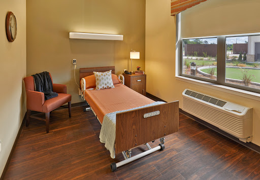 A serene and well-designed hospital patient room featuring a bed, a comfortable chair, and ample natural light.