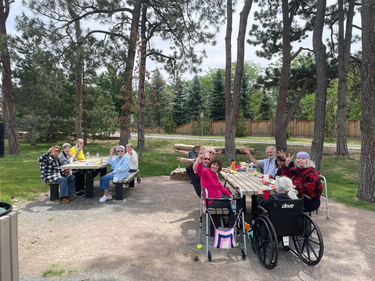 A group of elderly people enjoying a picnic outdoors surrounded by trees.