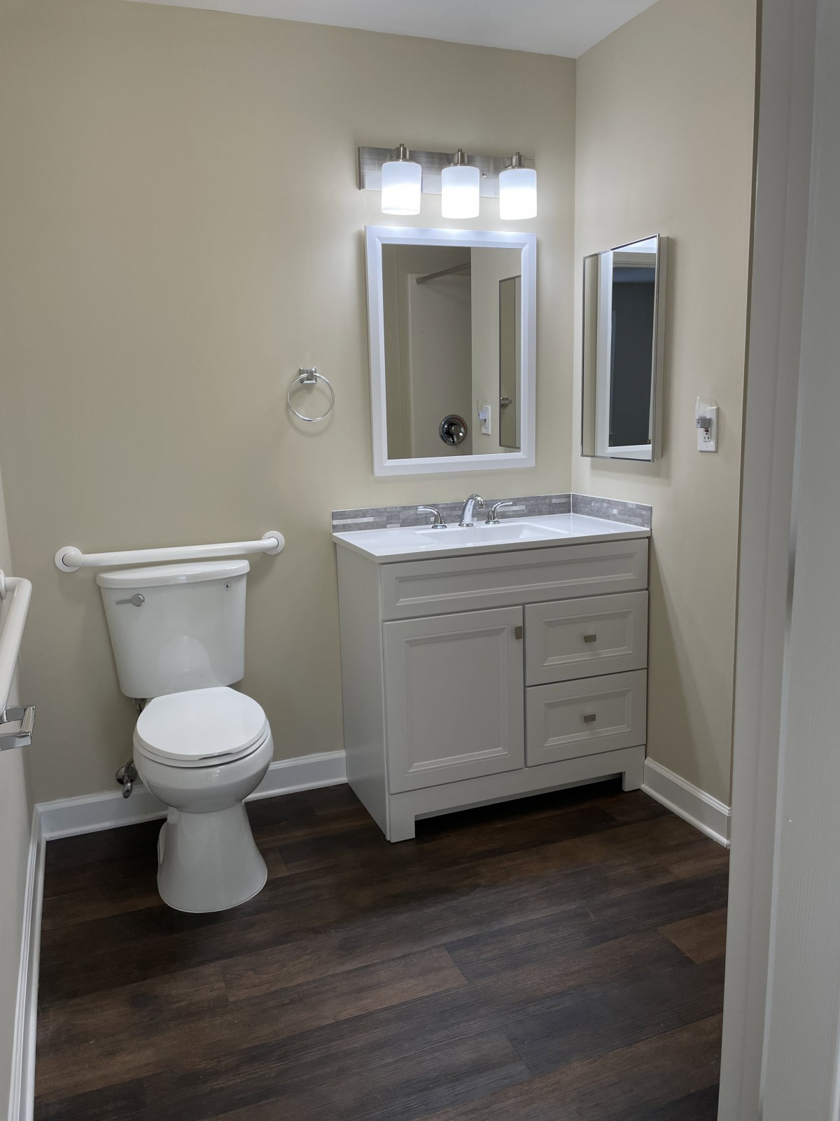 A modern bathroom with a toilet, sink, and vanity featuring a mirror and wood flooring.