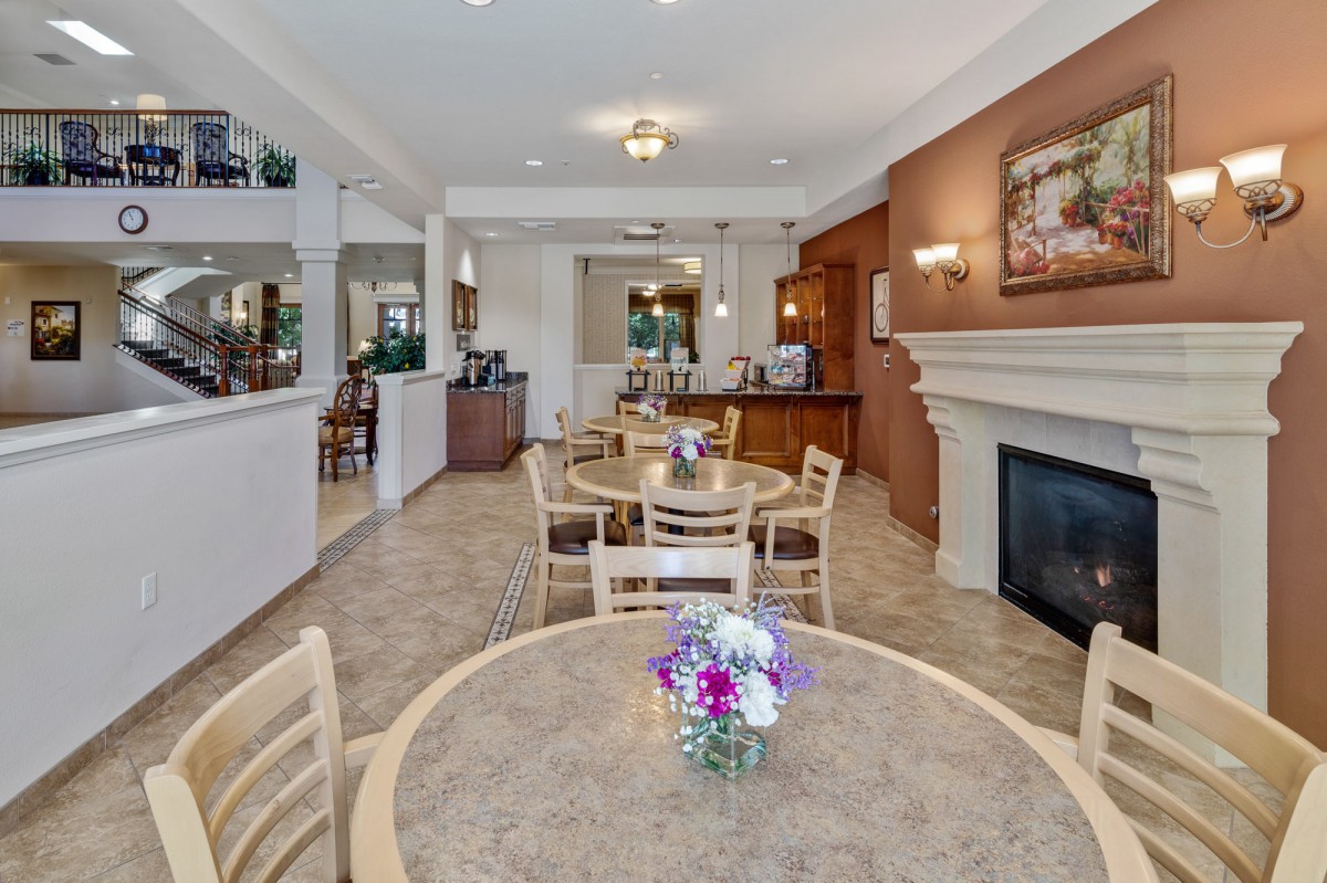 A cozy dining area with tables and chairs, featuring a fireplace and floral decorations.