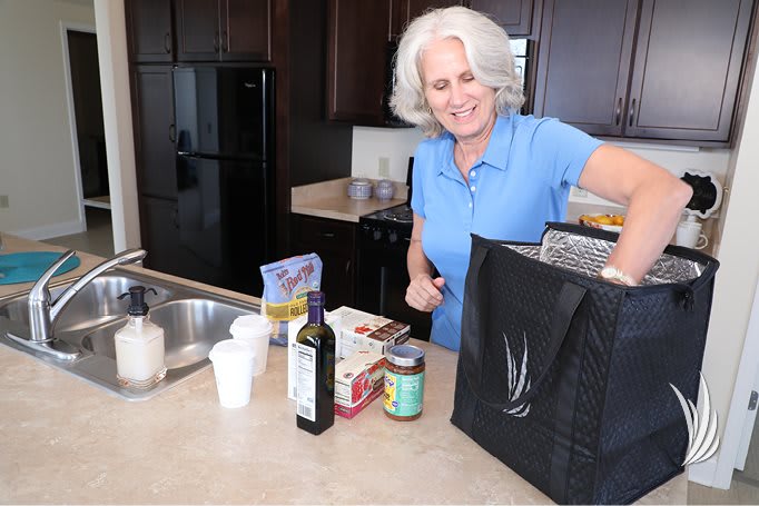 A woman unpacking groceries in the kitchen, smiling while sorting items from a shopping bag.