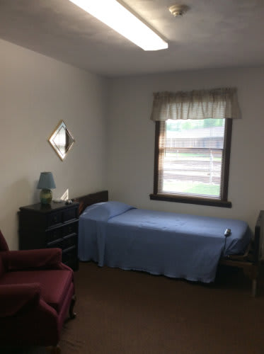 A simple bedroom with a single bed, a dresser, and a window.