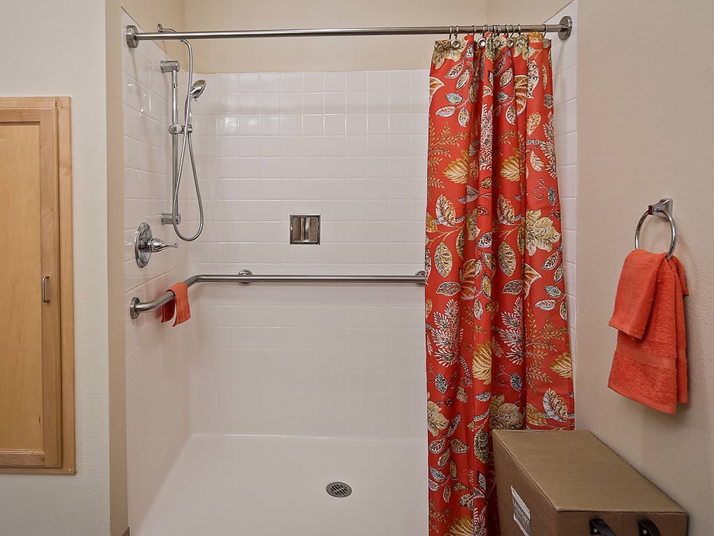 A bathroom shower with an orange floral-patterned curtain and matching towel.